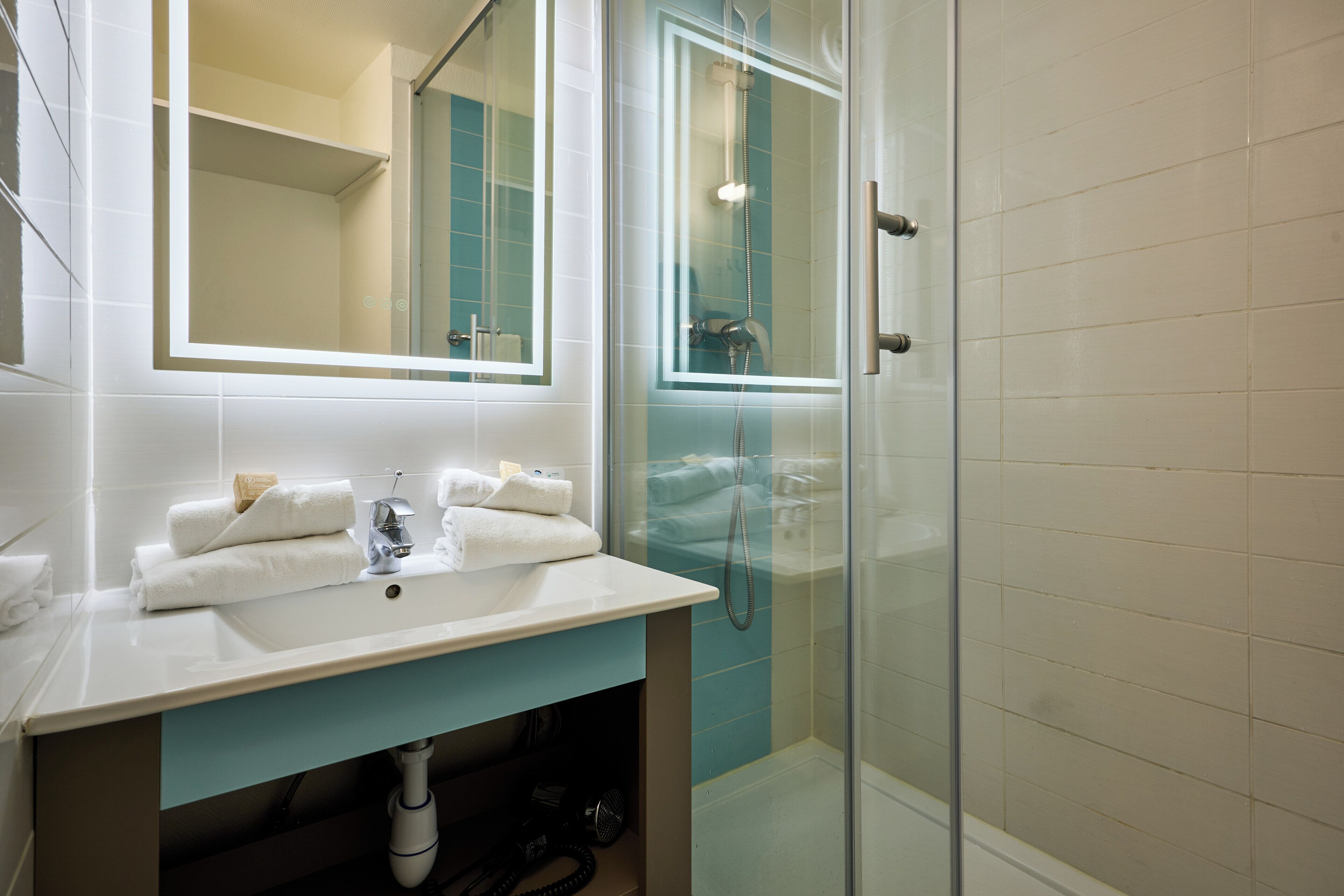 A bathroom with a white sink, a mirror, a glass shower enclosure, and a towel rack.