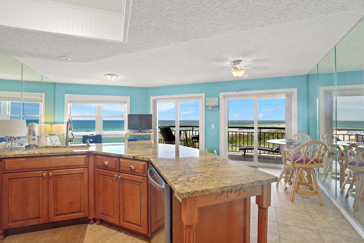 A kitchen with a large island, a dining area with chairs, and a view of the ocean through large windows.