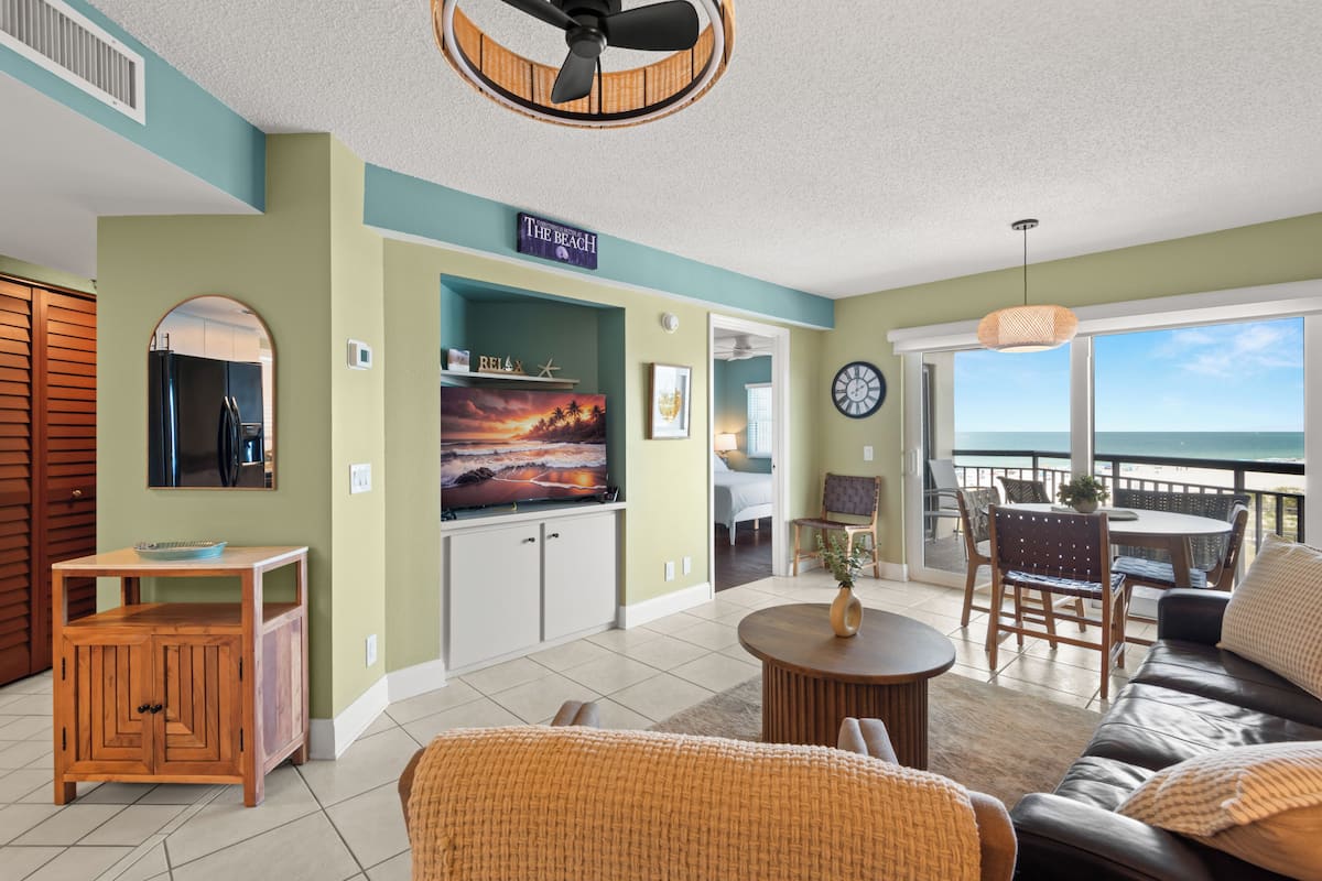 A living room with a TV, wooden cabinet, wicker furniture, and a view of the ocean.