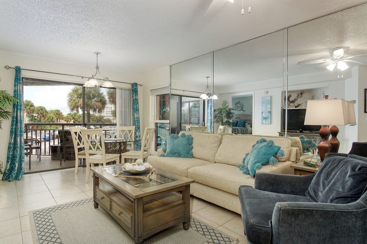 A living room with a sofa, armchair, coffee table, and a dining area with chairs and a table.