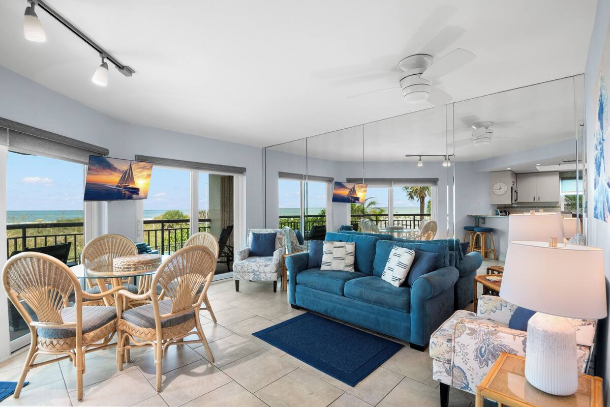 A spacious living area with a blue sofa, wicker chairs, a glass table, and a view of the ocean.
