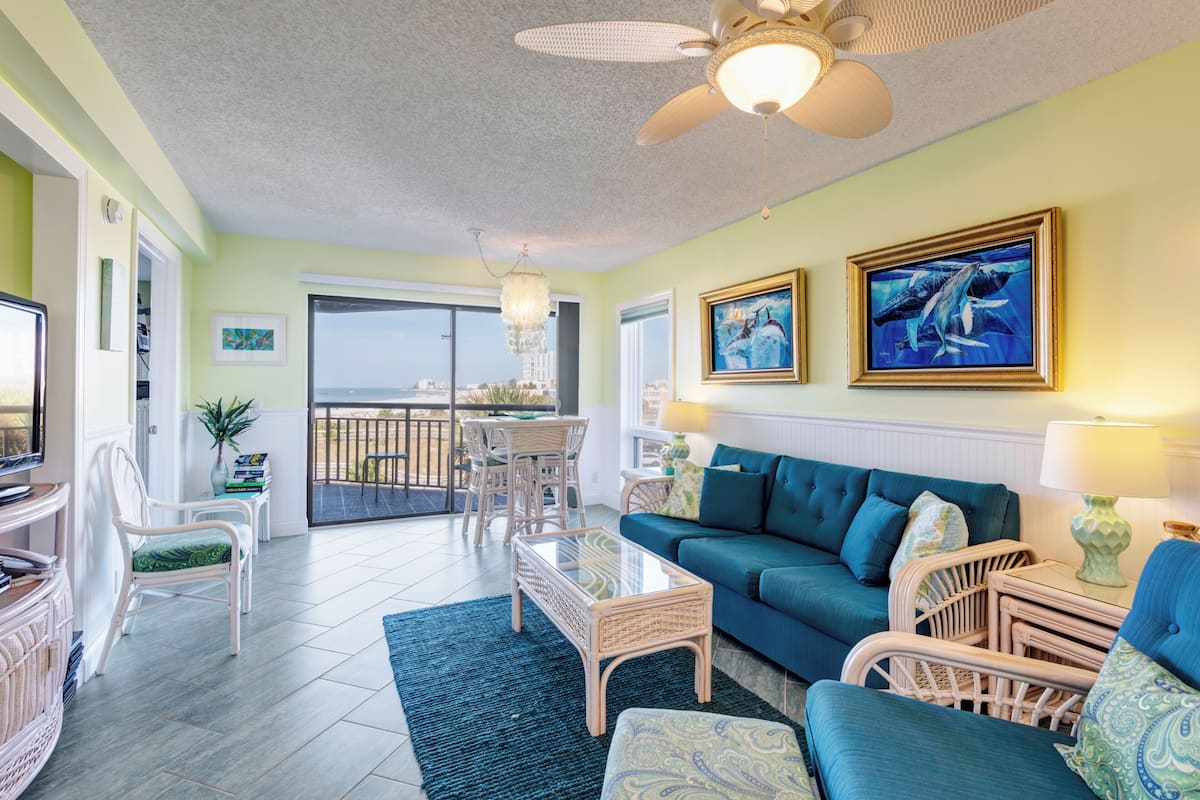 A living room with a blue sofa, wicker furniture, a glass coffee table, and a ceiling fan.