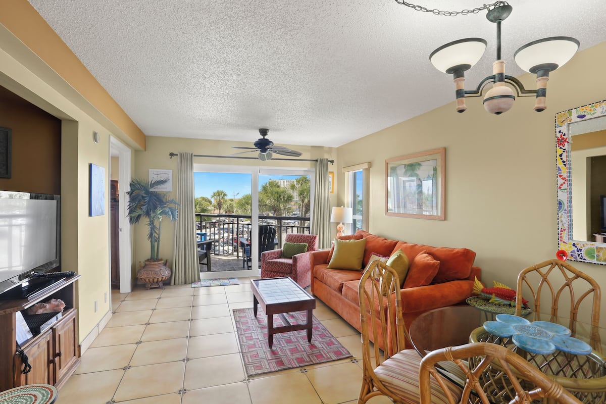 A living room with a sofa, chairs, a coffee table, a television, and a balcony with a view.