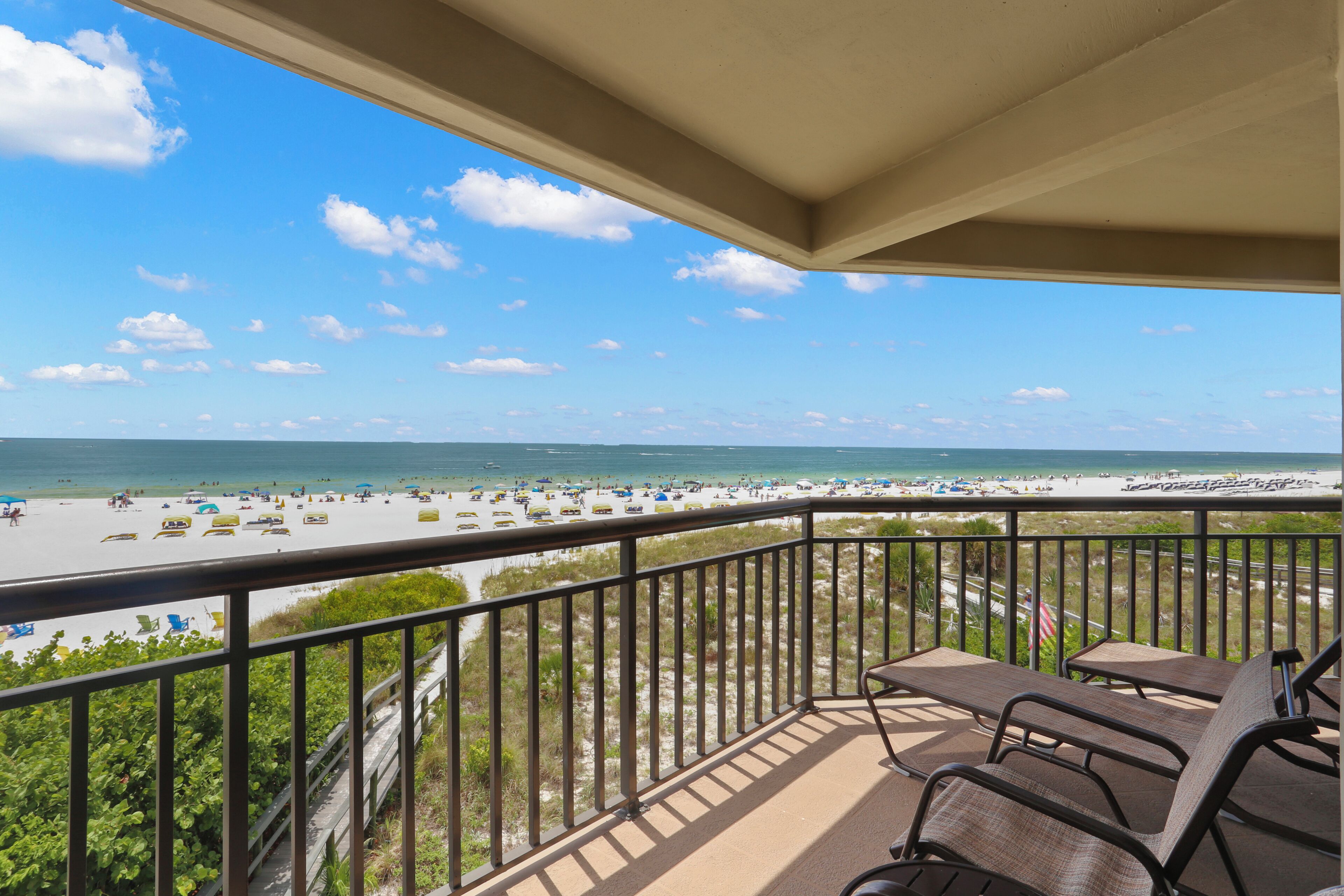 A balcony with a view of a beach, outdoor seating, and a railing.