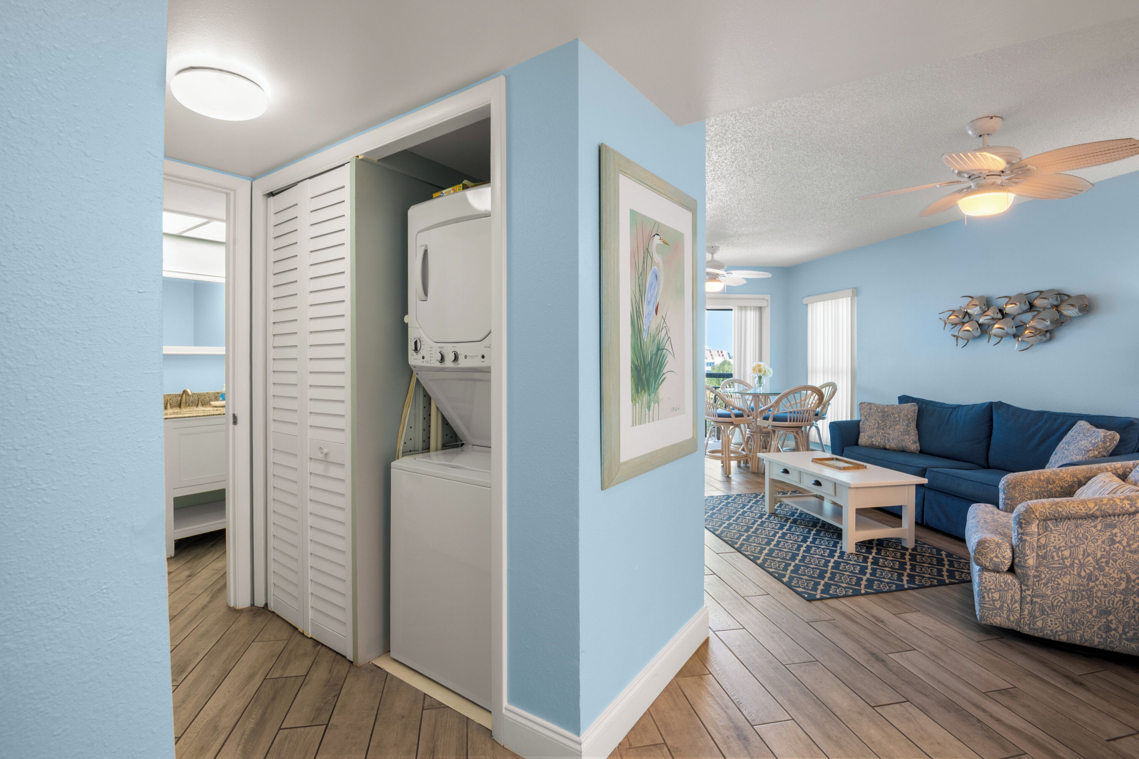 Una habitación con pared azul, armario blanco, ventilador de techo y sofá azul.