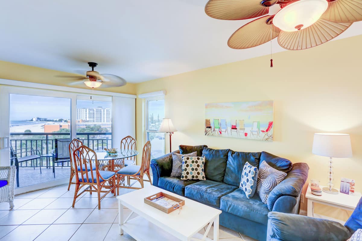 A living room with a sofa, chairs, a coffee table, a balcony with a view, and ceiling fans.