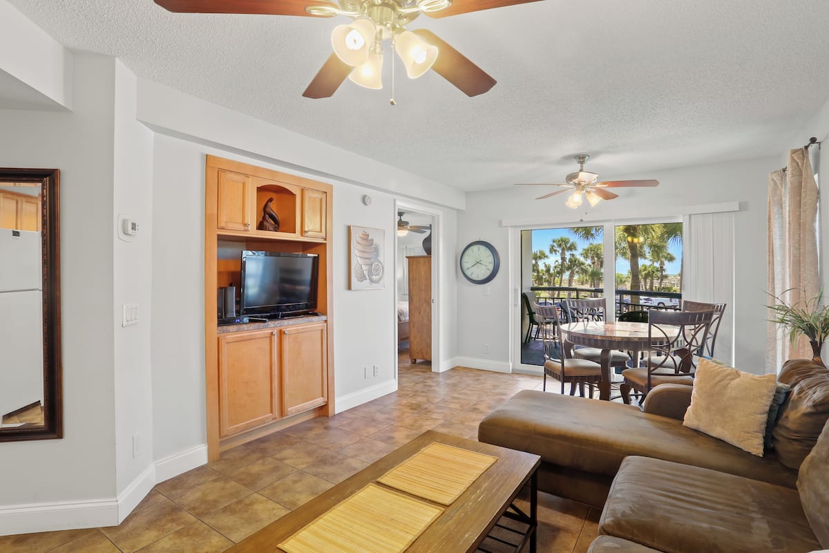 A spacious living area with a large brown leather sofa, wooden cabinets, a television, and a ceiling fan.