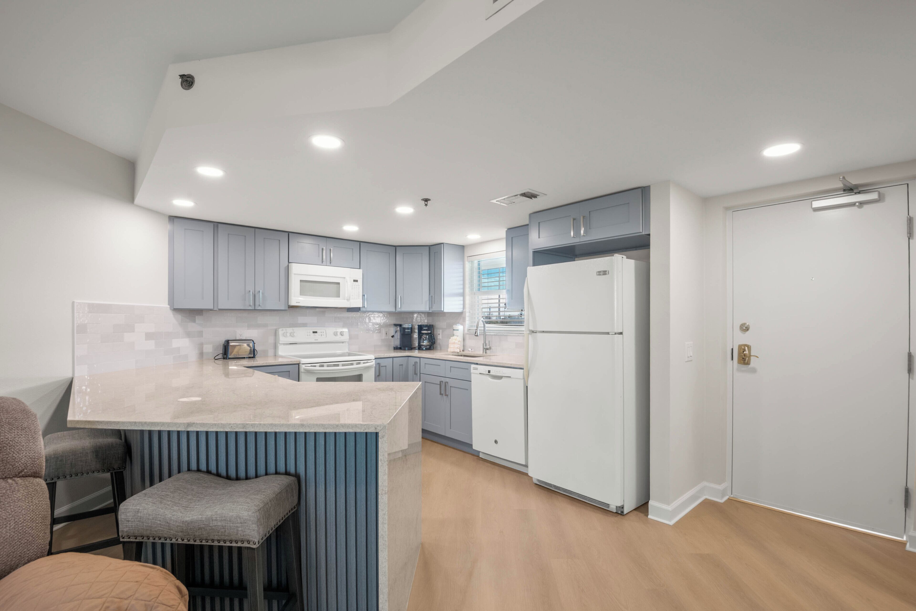 Una cocina moderna con armarios grises, un refrigerador blanco, un microondas y una isla integrada con taburetes de bar.