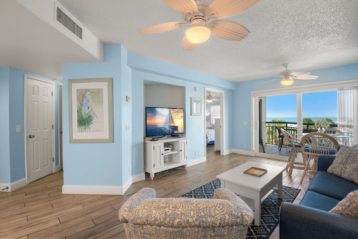 A living room with a TV, ceiling fan, and a view of the outdoors.