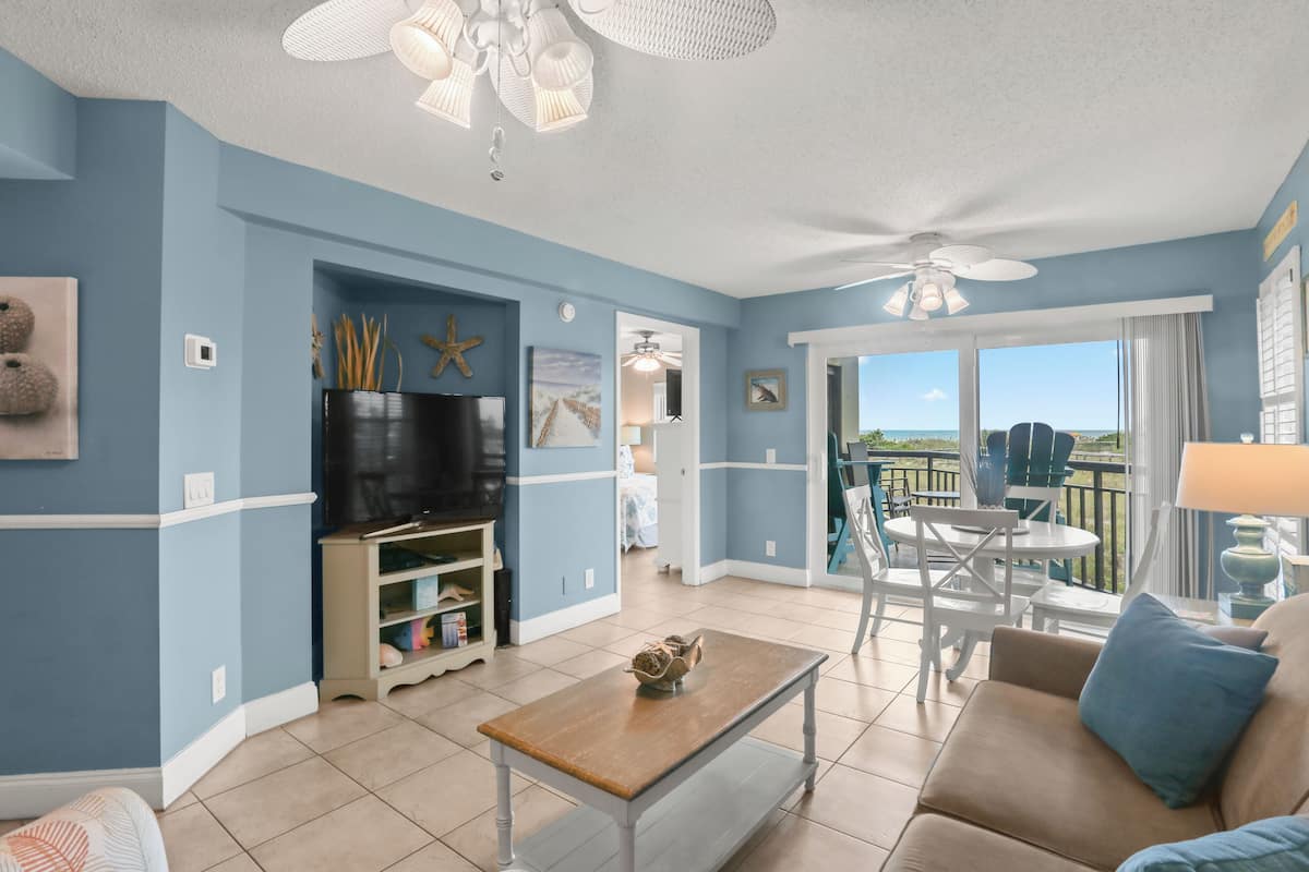 A living room with a TV, bookshelf, and a balcony with outdoor furniture.