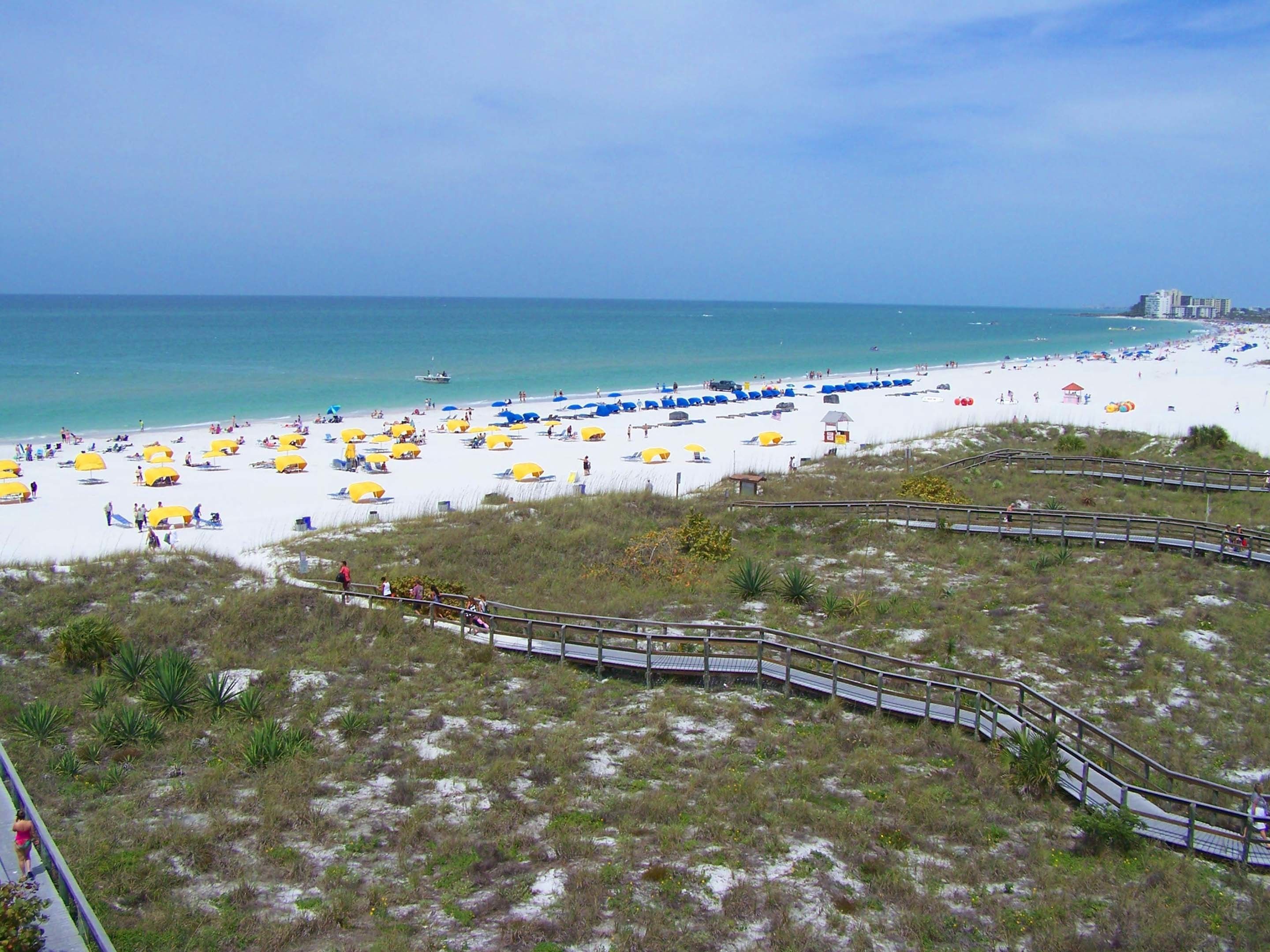 A beach with a wooden boardwalk leading to the shore, surrounded by dunes and sparse vegetation.