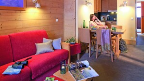 Una habitación acogedora con un sofá rojo, una mesa de comedor y una zona de cocina.