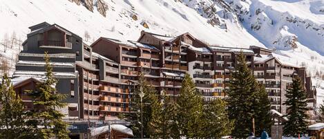 Ein mehrstöckiges Hotel mit Balkonen, umgeben von schneebedeckten Bergen.