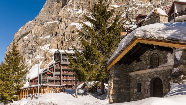 Un albergue de montaña con fachada de piedra, balcones de madera y paisajes nevados.