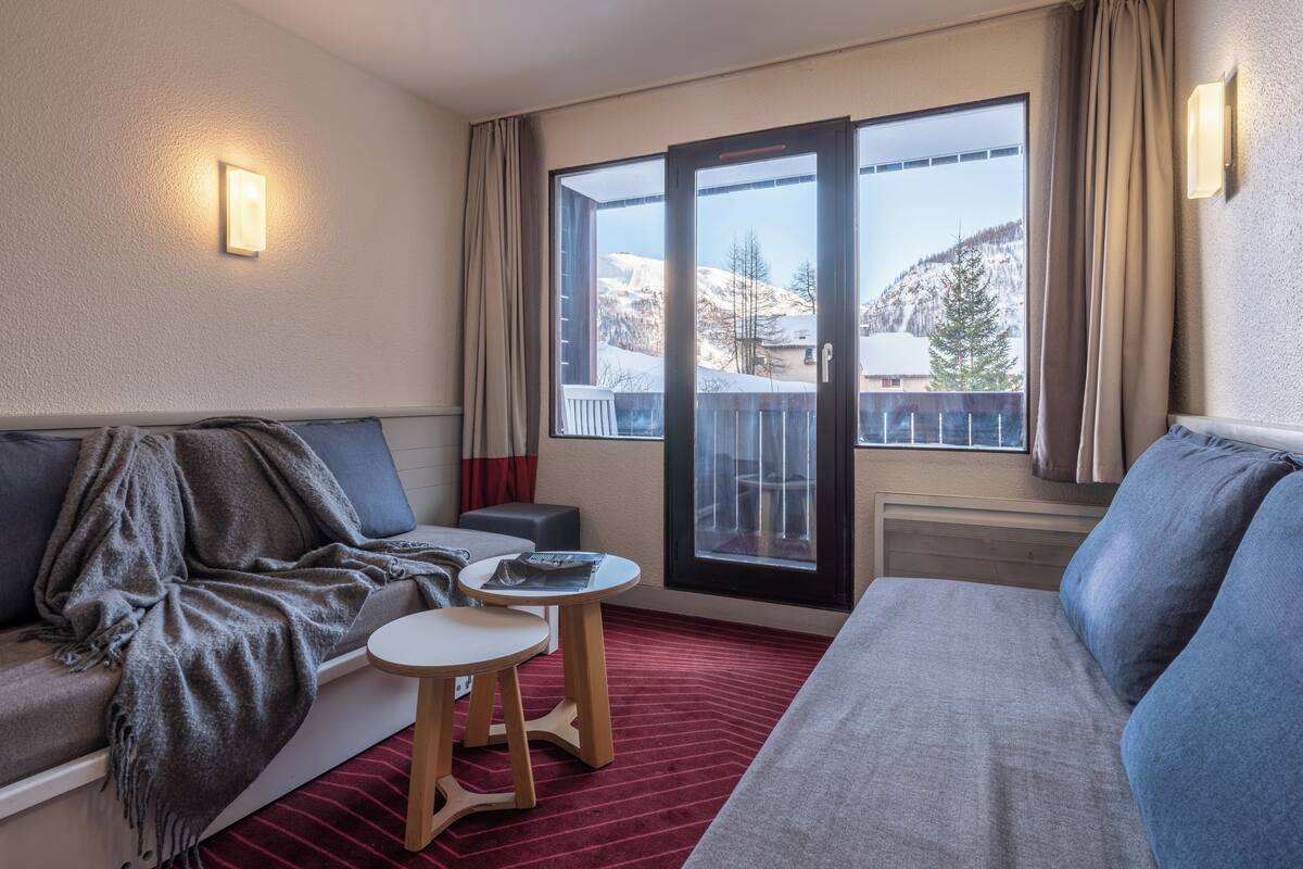 Une chambre d’hôtel avec un canapé, une petite table, une fenêtre donnant sur les montagnes et une porte coulissante.