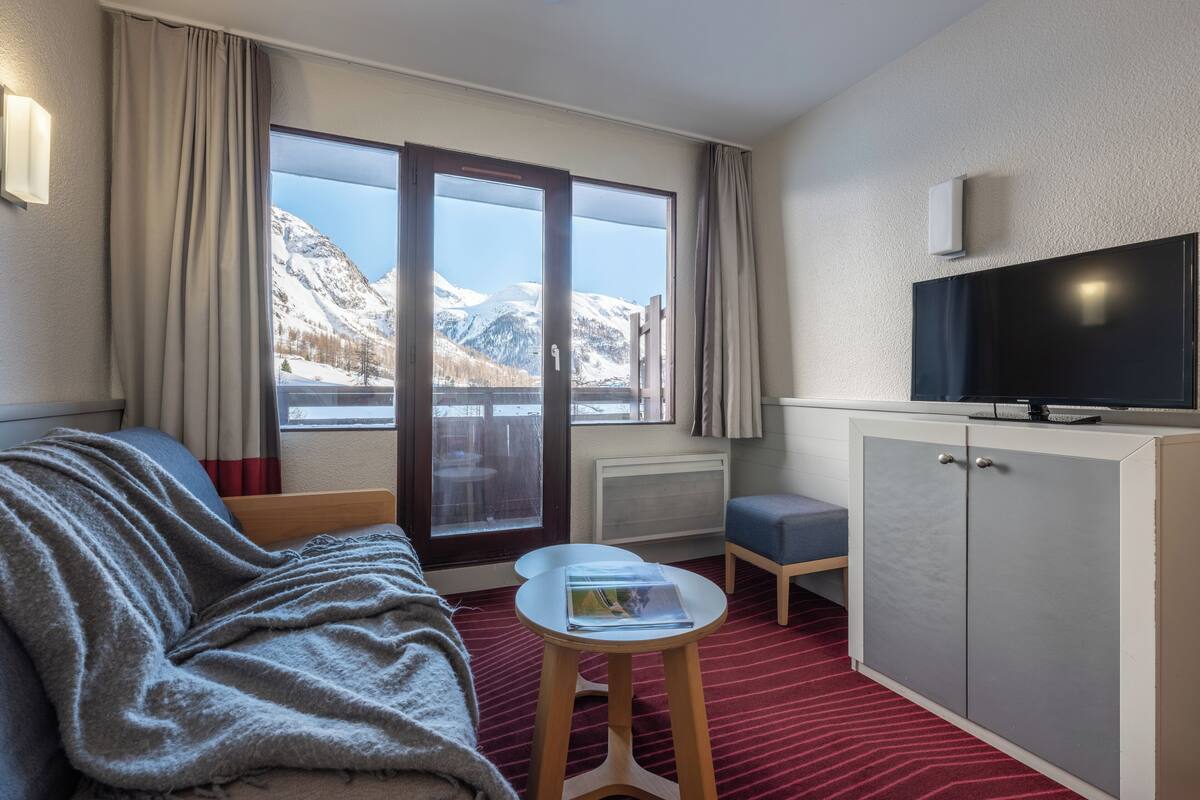 Une chambre d’hôtel comprenant un lit, une télévision, une petite table, une armoire et une vue sur les montagnes, visible par une porte coulissante.
