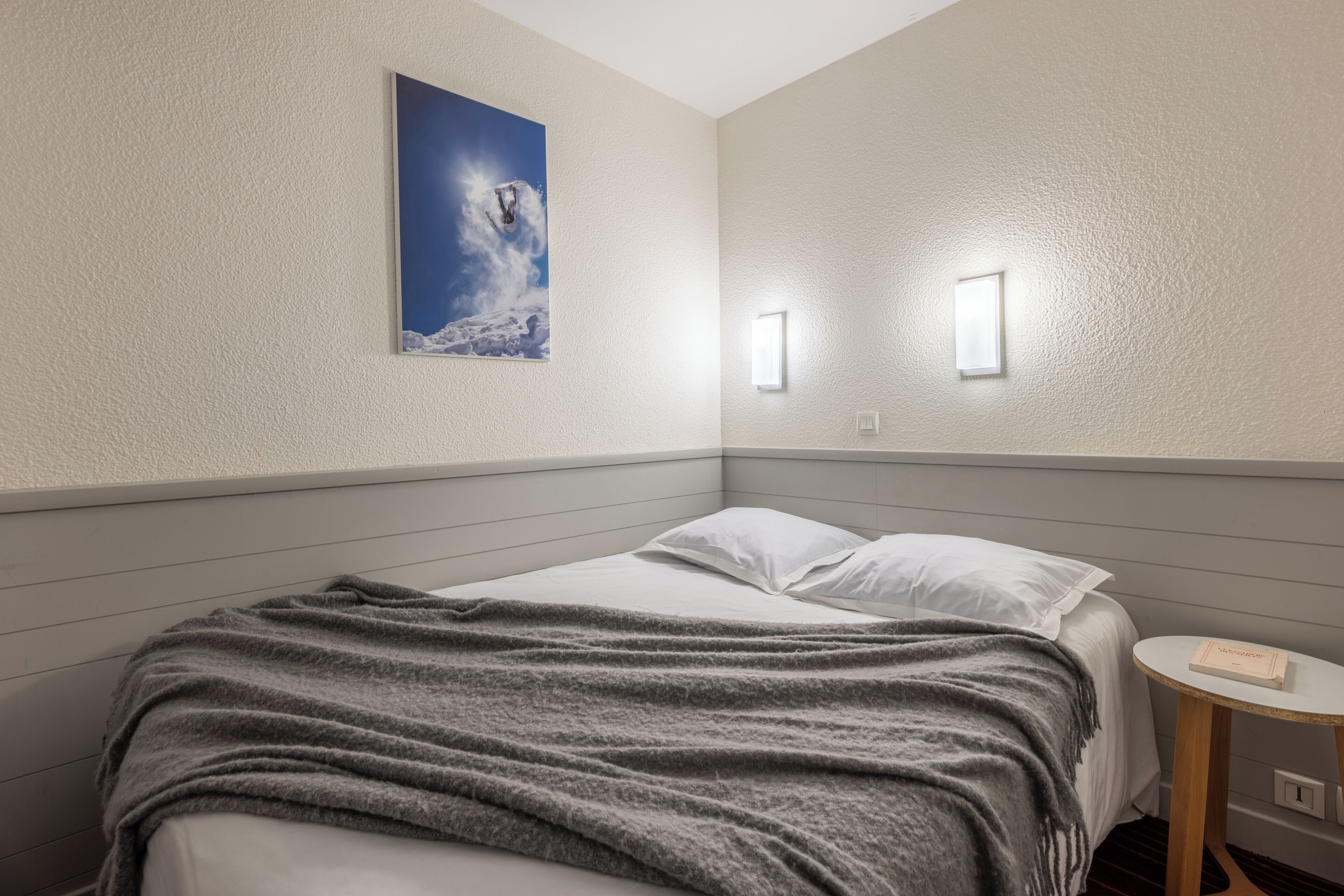 Ein Hotelzimmer mit einem Bett, einem Nachttisch, einer Wandleuchte und einem gerahmten Bild.