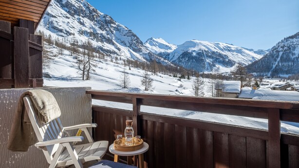 A wooden deck with a chair and table, overlooking a snowy mountain landscape. - Résidence Pierre & Vacances La Daille (Val-d'Isere)