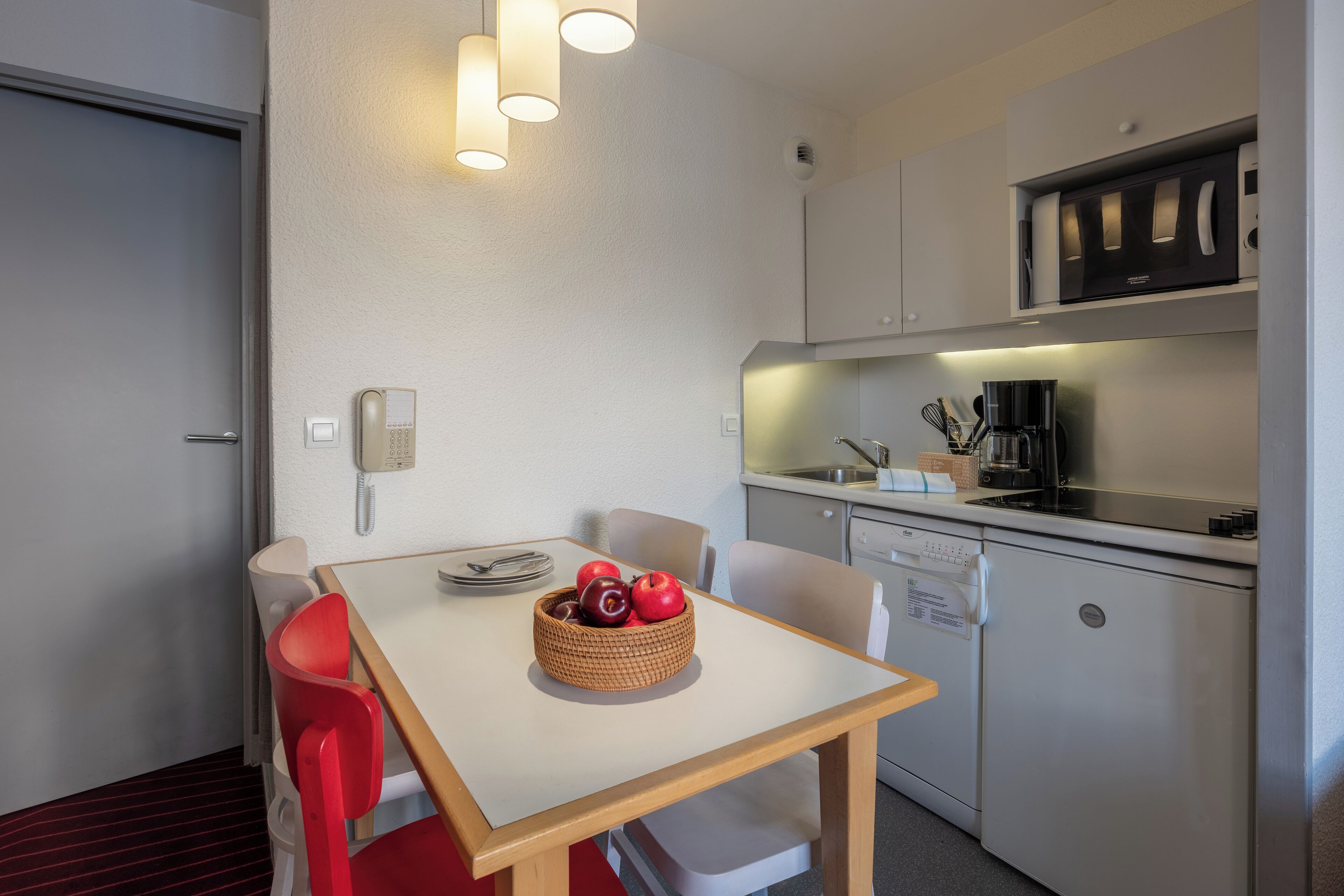 A compact kitchen with a dining table, chairs, and a fruit bowl.