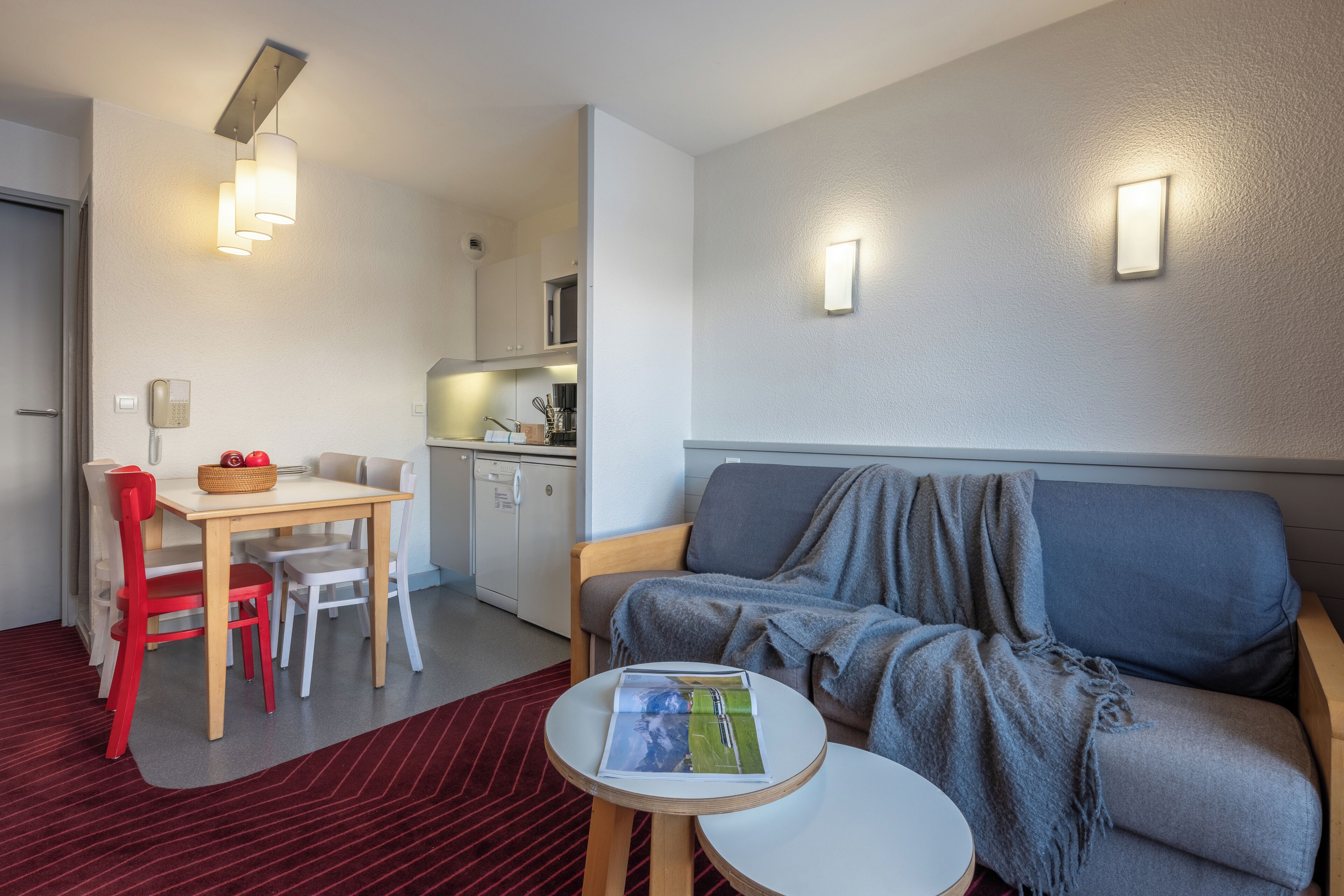 A compact living space with a dining area, kitchenette, and a sofa with a blanket.