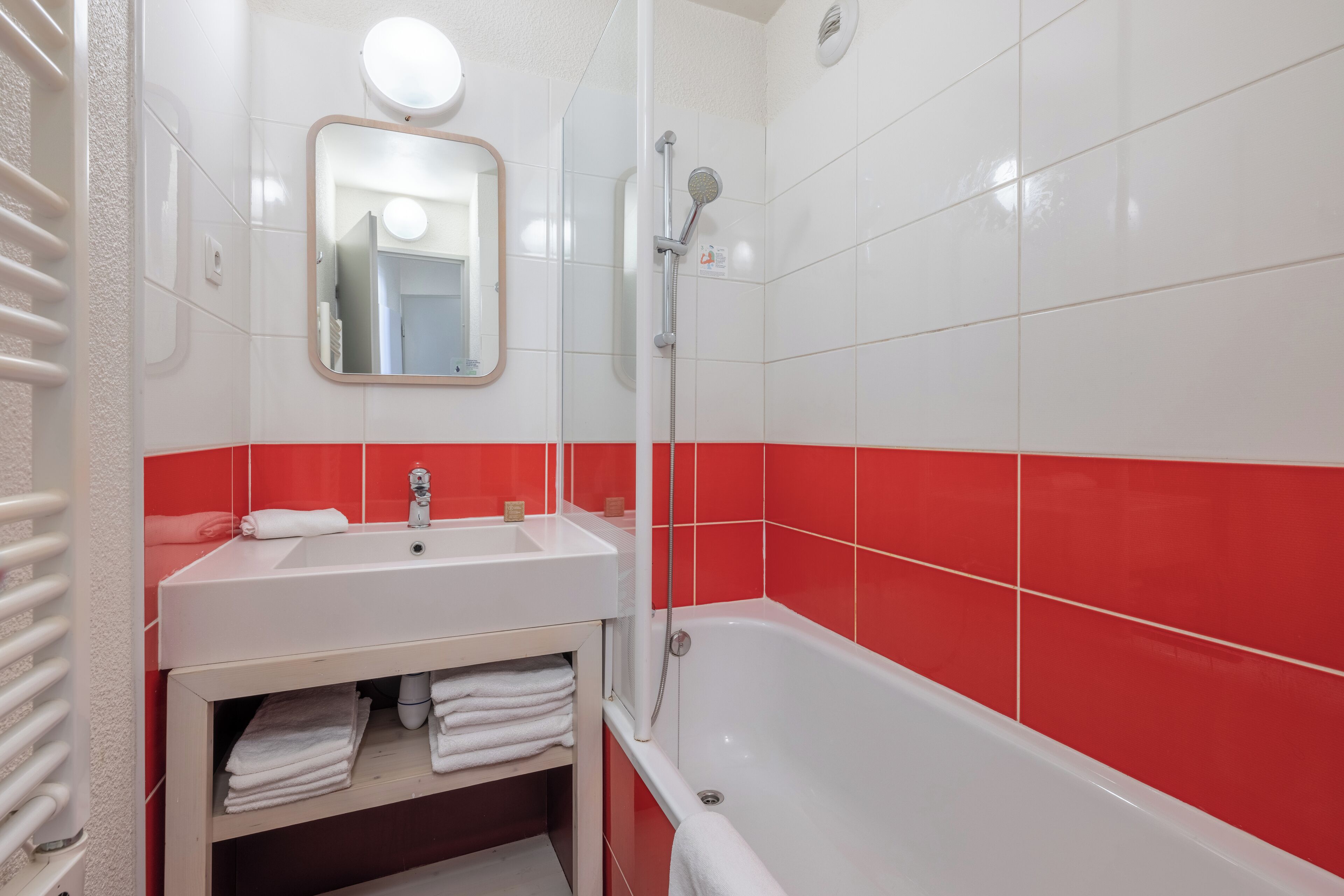 A bathroom with a white sink, a mirror, a shower, and red-tiled walls.