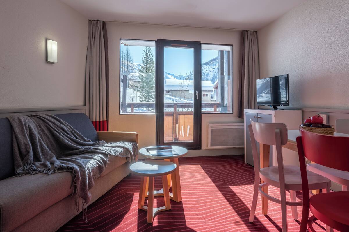 Une chambre d’hôtel avec un canapé, une petite table, un téléviseur et une vue sur les montagnes, visible à travers une grande fenêtre.