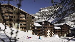 A multi-story hotel with wooden balconies and snow-covered roofs, set against a mountainous backdrop.