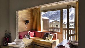 A cozy room with a wooden wall, a sofa, a small table, and a window with a view of a snowy mountain.