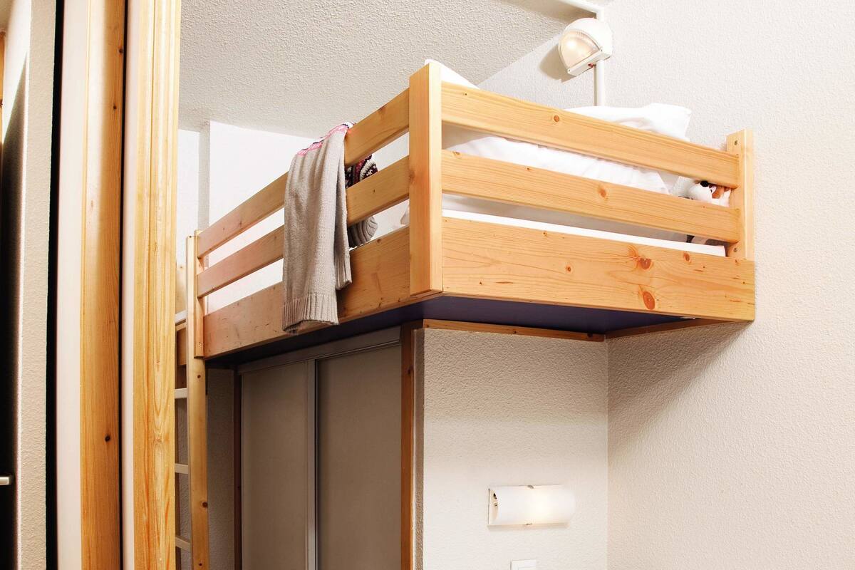 Ein Schlafraum mit Etagenbetten, einer Holzleiter, einem Nachttisch mit einer rosafarbenen Ablage und einer Zeitschrift auf dem Bett.