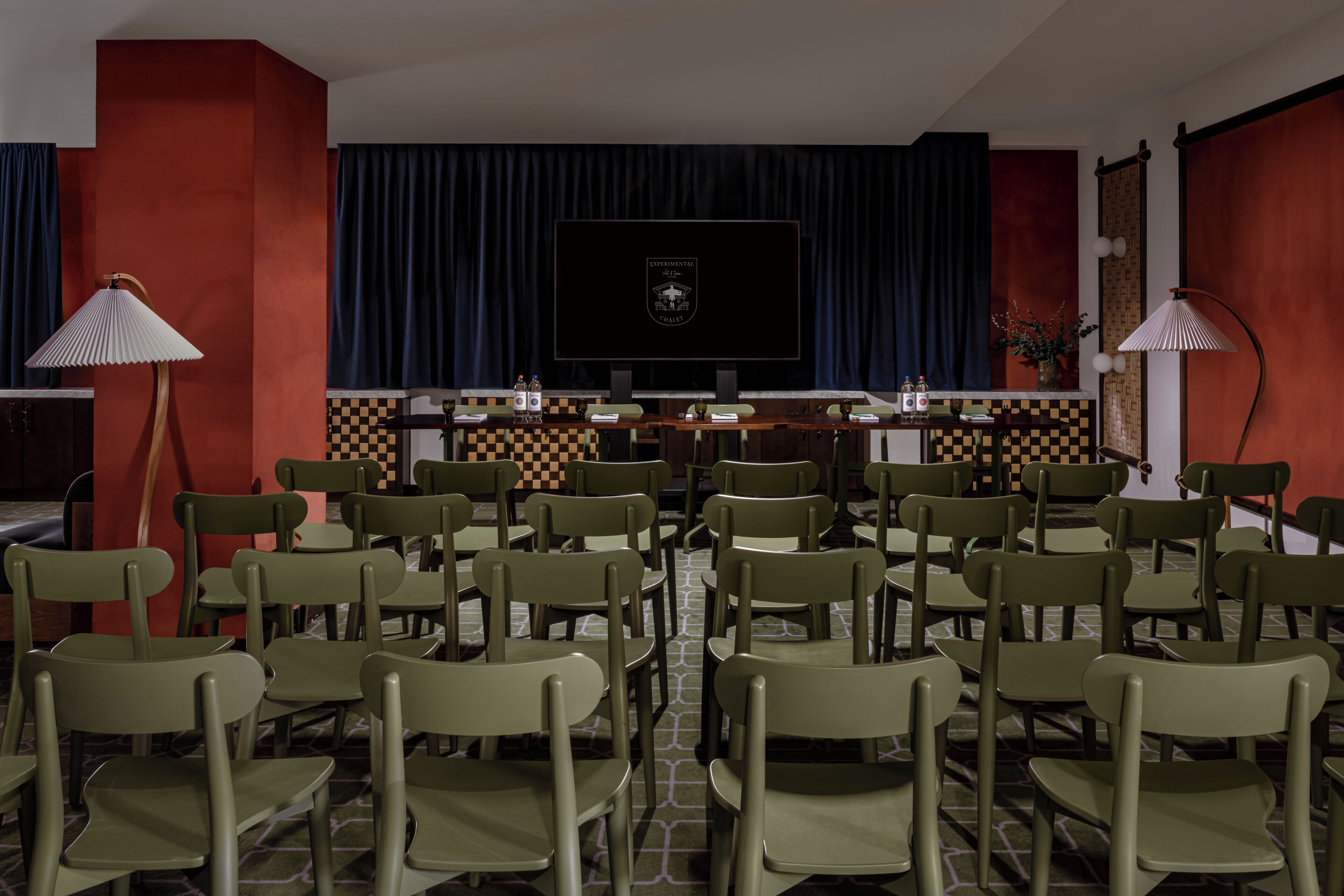 A conference room with a large screen, green chairs, and a checkered floor pattern.