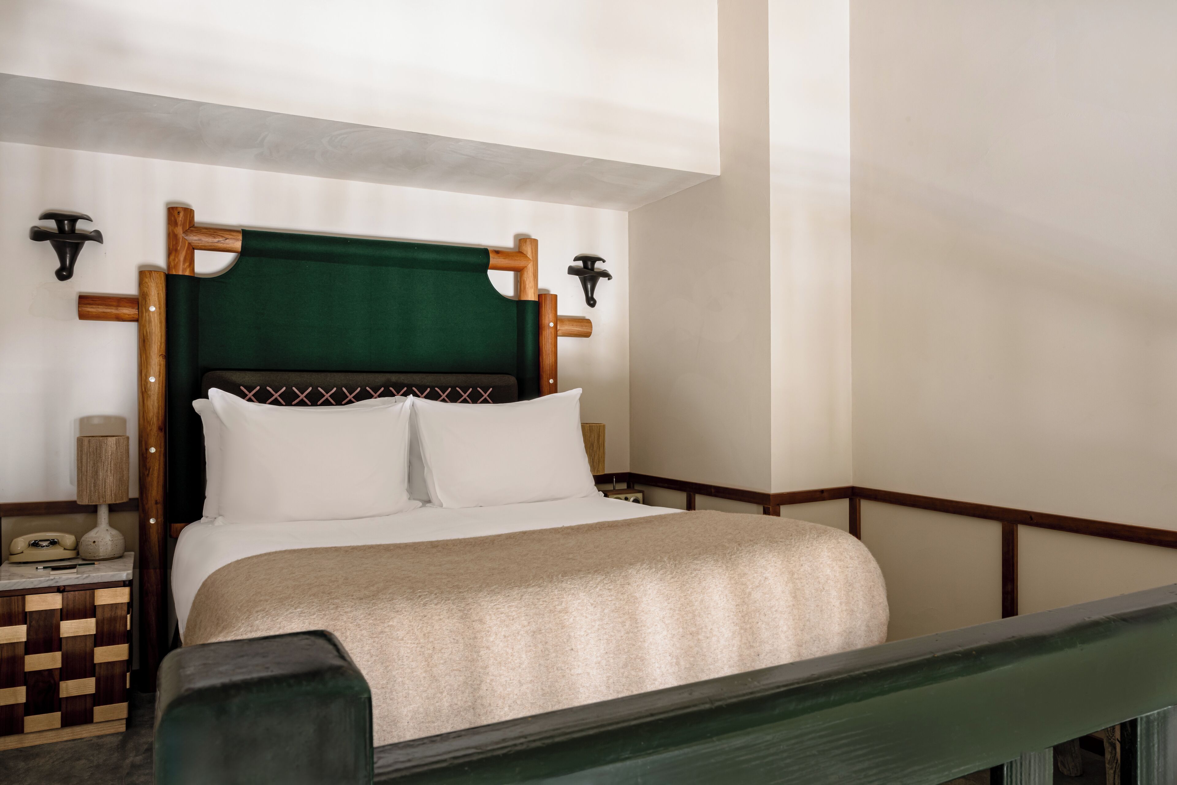 A neatly made bed with a green headboard, a bedside table with a lamp, and a checkered nightstand.
