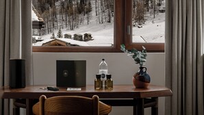 Un escritorio de madera con una silla, una botella de perfume, un pequeño florero con una planta y una caja.