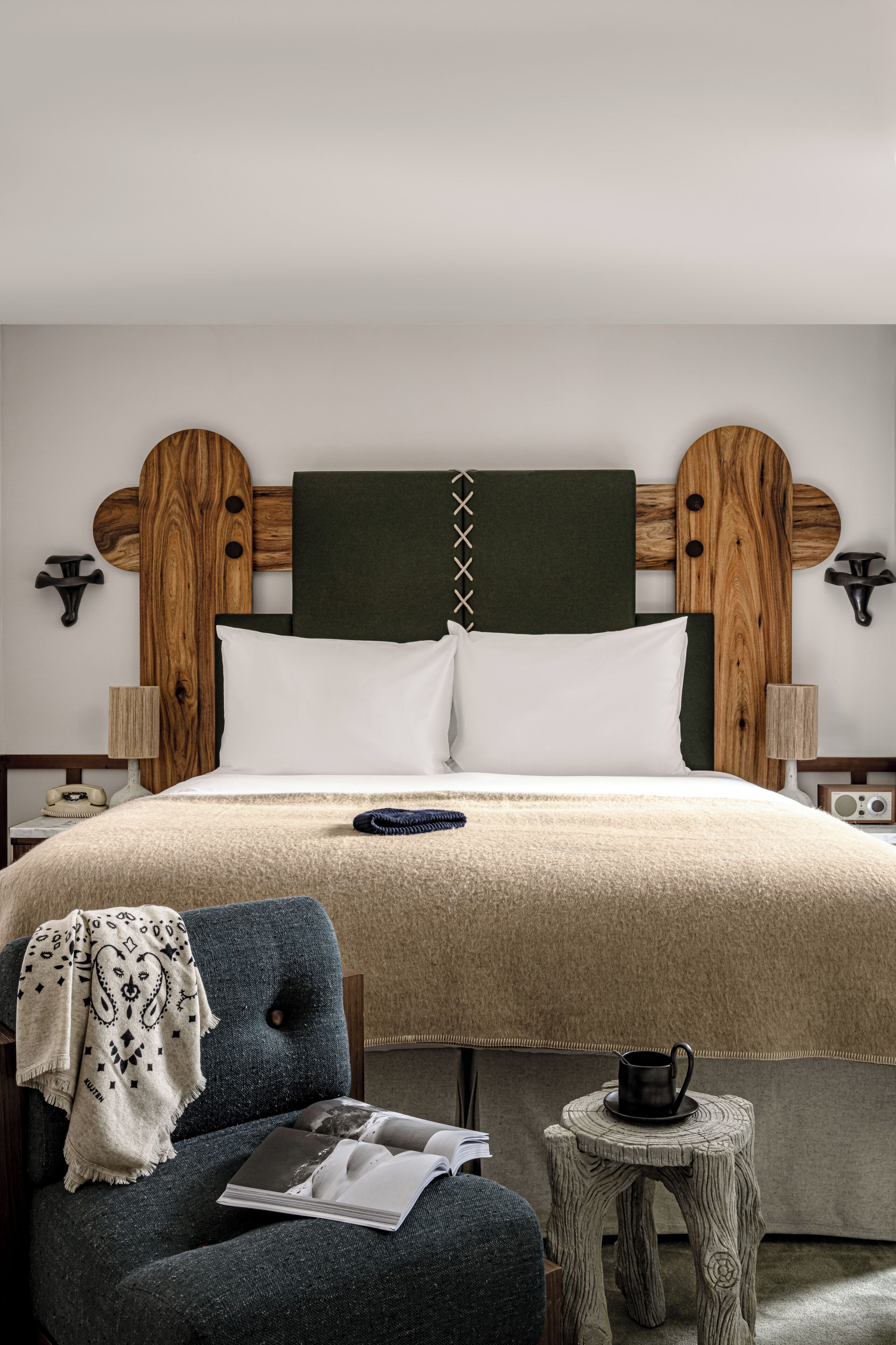 Une chambre à coucher bien rangée, avec un grand lit, une chaise, une petite table et une lampe fixée au mur.