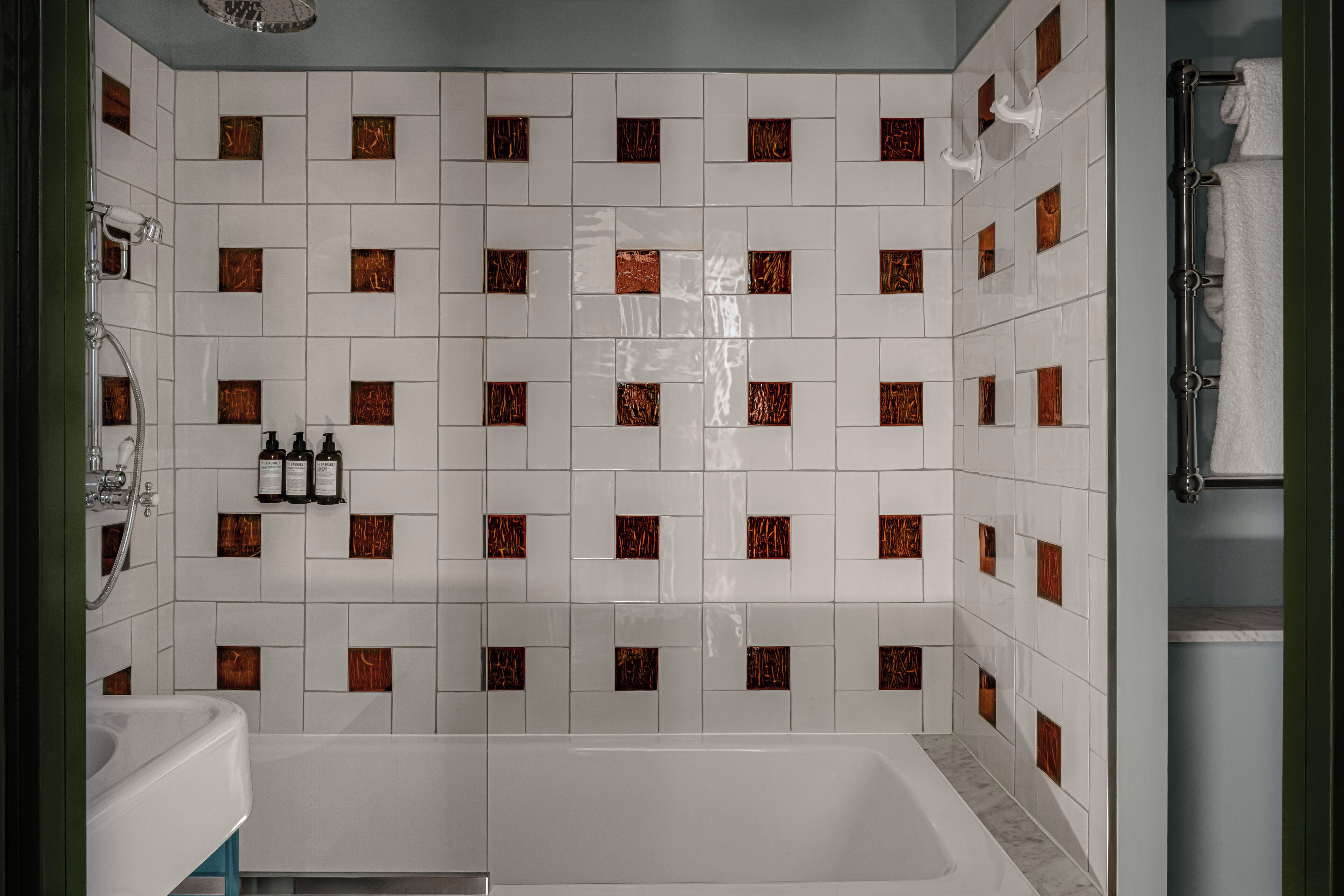 A bathroom with white tiles and brown accents, a bathtub, a sink, and a towel rack.