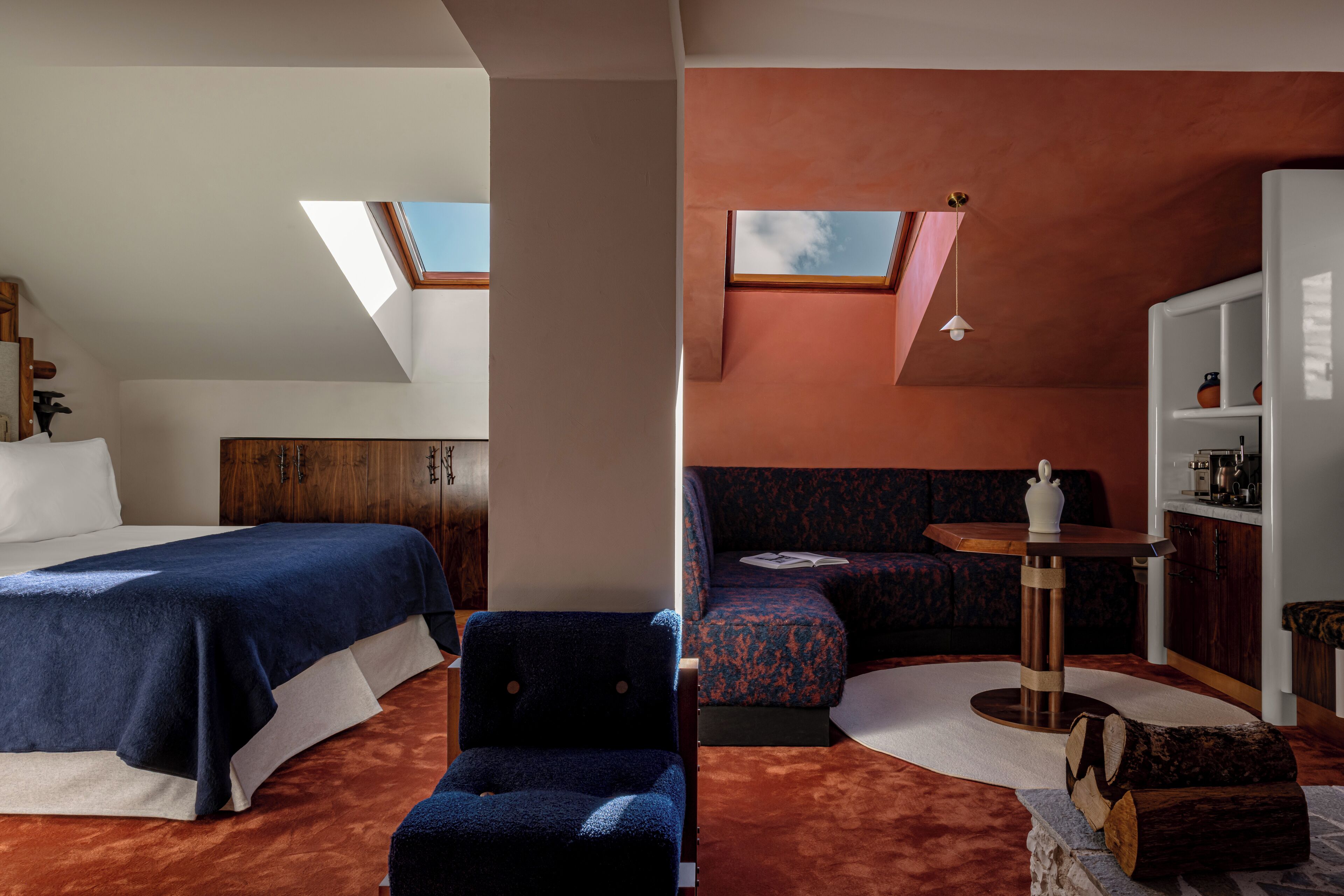 A room with a bed, a chair, a sofa, a small table, and a bookshelf. There are skylights on the ceiling.