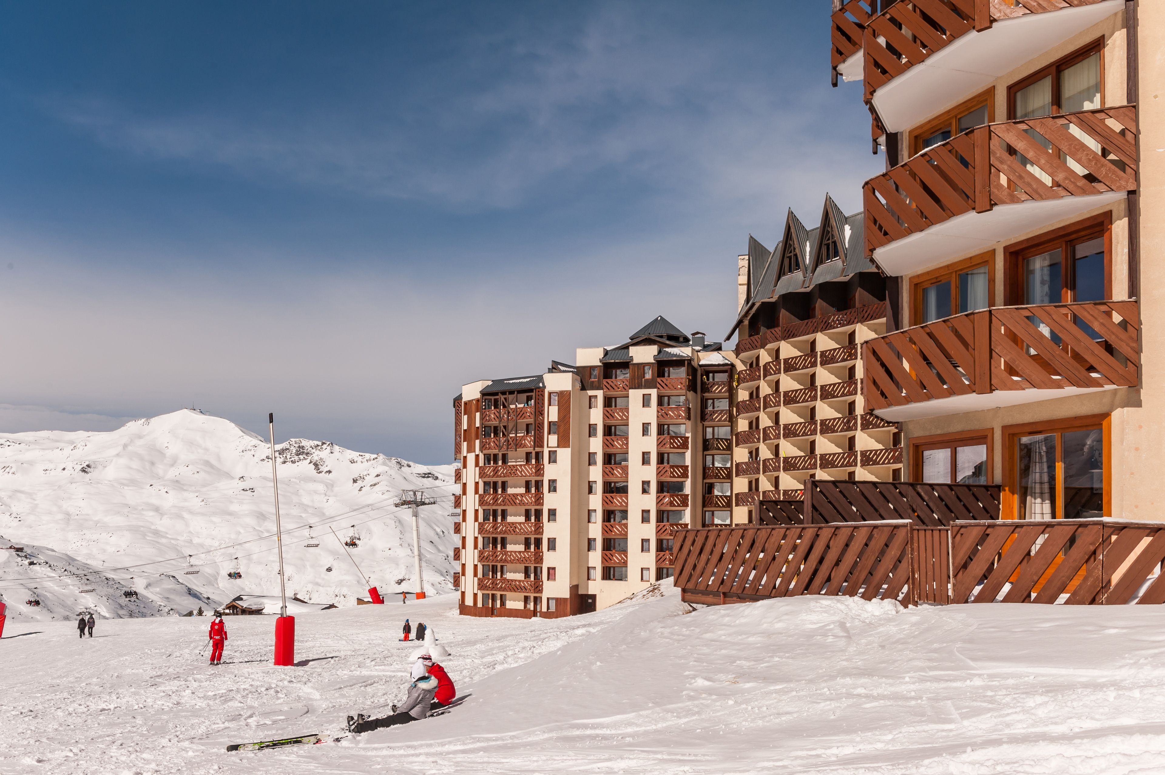 Estación de esquí cubierta de nieve con un edificio de varios pisos que cuenta con balcones y pistas de esquí al fondo.