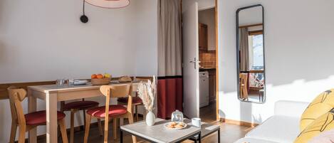 A modern living room with a dining area, wooden furniture, a mirror, and a view into the kitchen.