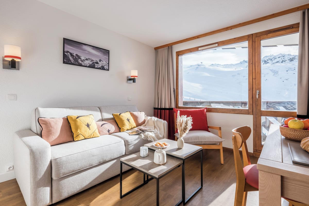 A modern living room with a sofa, coffee table, and a view of a snowy mountain.