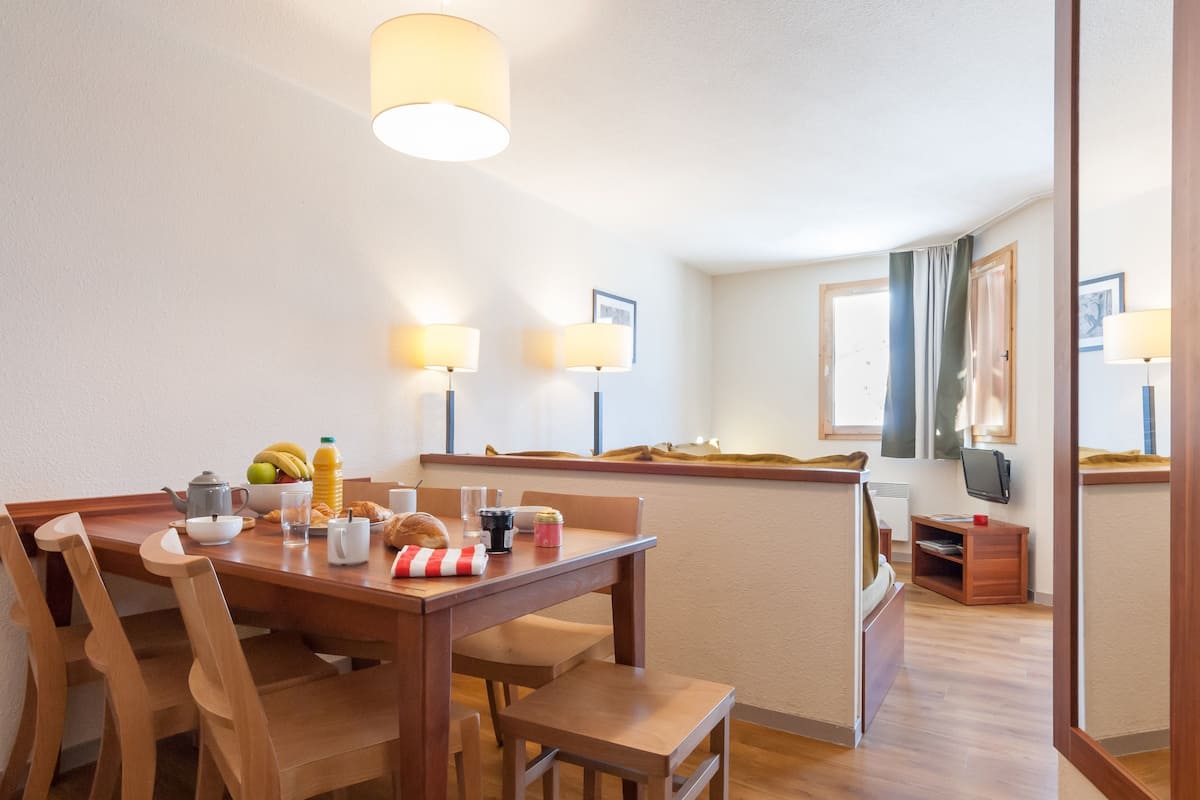 A dining area with a wooden table, chairs, and a breakfast setting including a teapot, cups, and a fruit bowl.