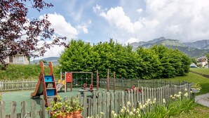 Un parque infantil con diversas estructuras de juego, rodeado de una valla de madera y abundante vegetación.