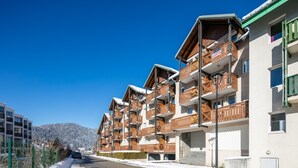 Fila de edificios de varios pisos con balcones, cielo azul despejado y una montaña nevada al fondo.