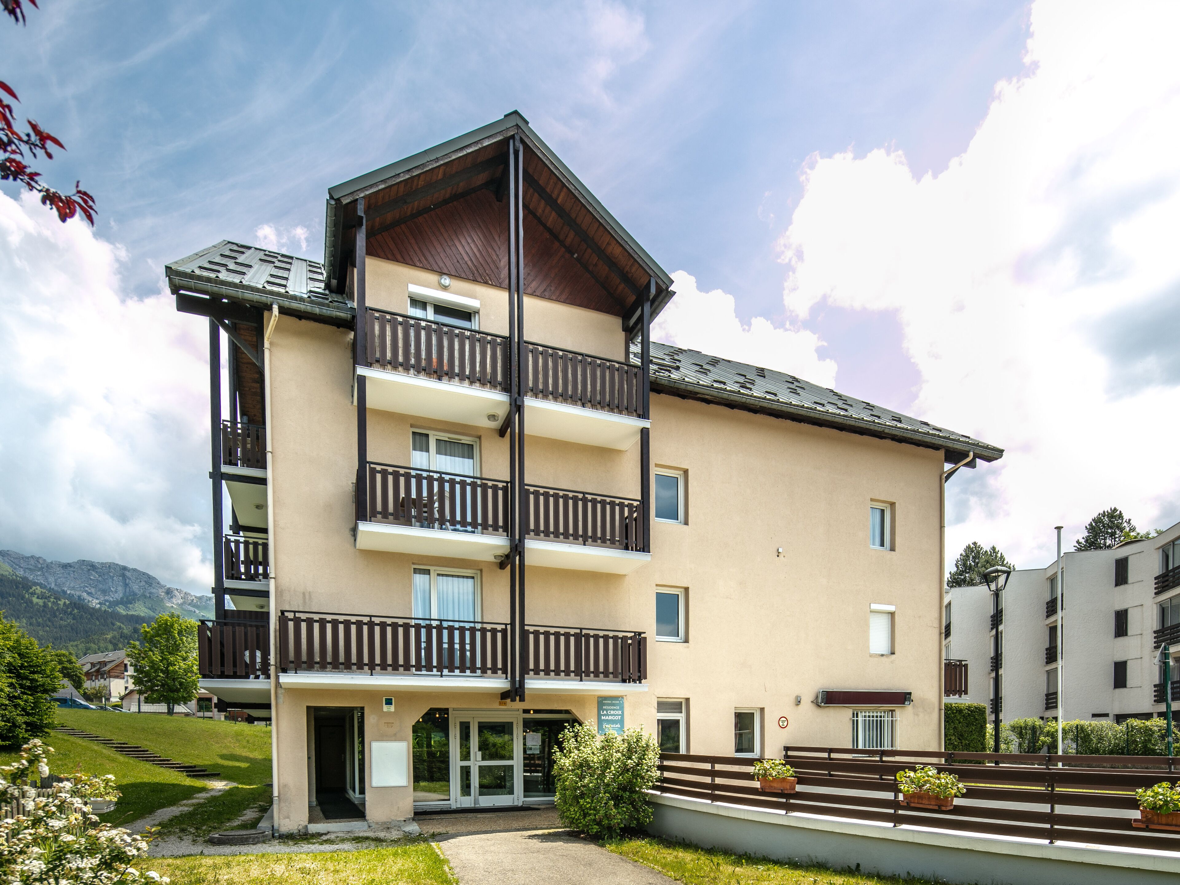 Un immeuble à plusieurs étages, doté de balcons, d’une entrée au niveau du sol et offrant une vue sur les montagnes en arrière-plan.