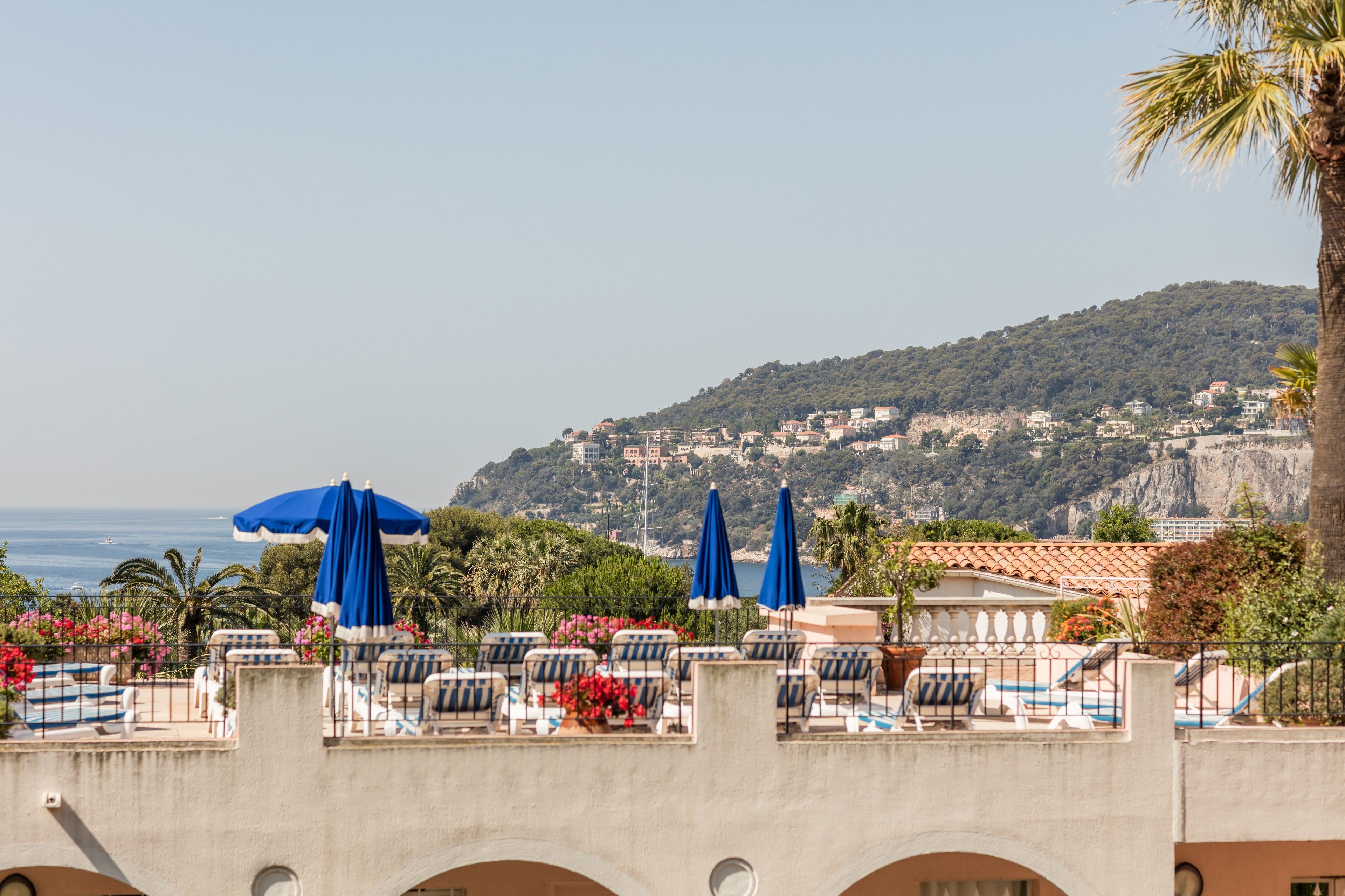 Een terras met loungezetels en parasols, met uitzicht op een kustplaats en de zee.