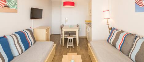 A compact living space with two sofas, a dining table, and a TV mounted on the wall.