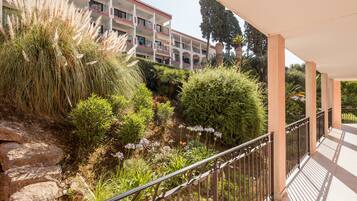 A balcony with a railing, a stone wall, and a building with balconies in the background.