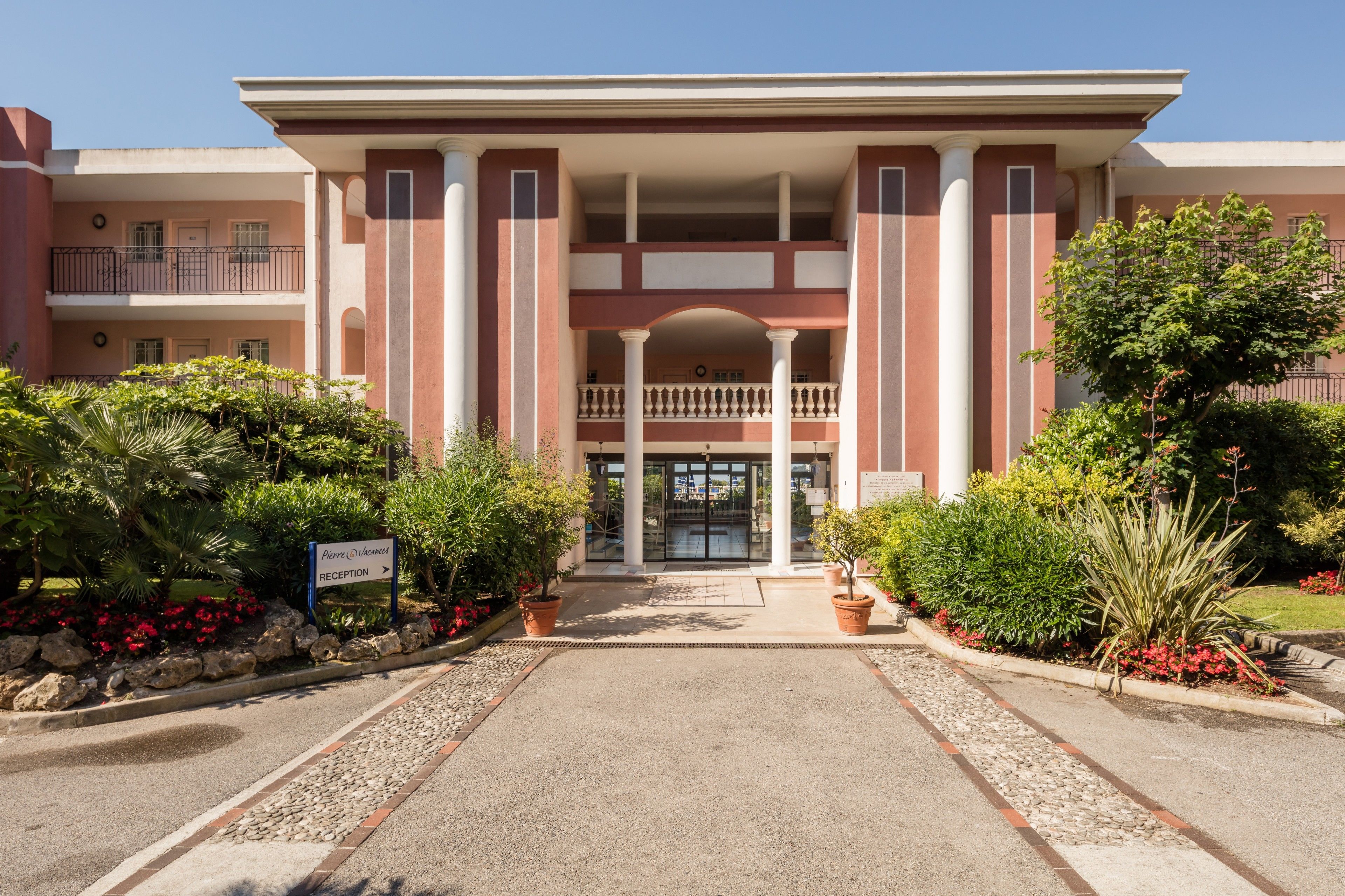 A hotel entrance with a reception area, a covered walkway, and a landscaped garden.