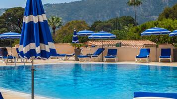 Una piscina con sombrillas azul y blanco a rayas, sillas de descanso y montañas al fondo.