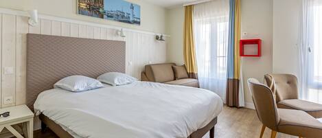 A hotel room with a large bed, a chair, a small table, and a painting on the wall.