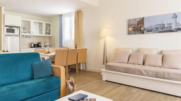 Un salon moderne avec un canapé turquoise, un canapé blanc et un coin repas comprenant une table et des chaises.