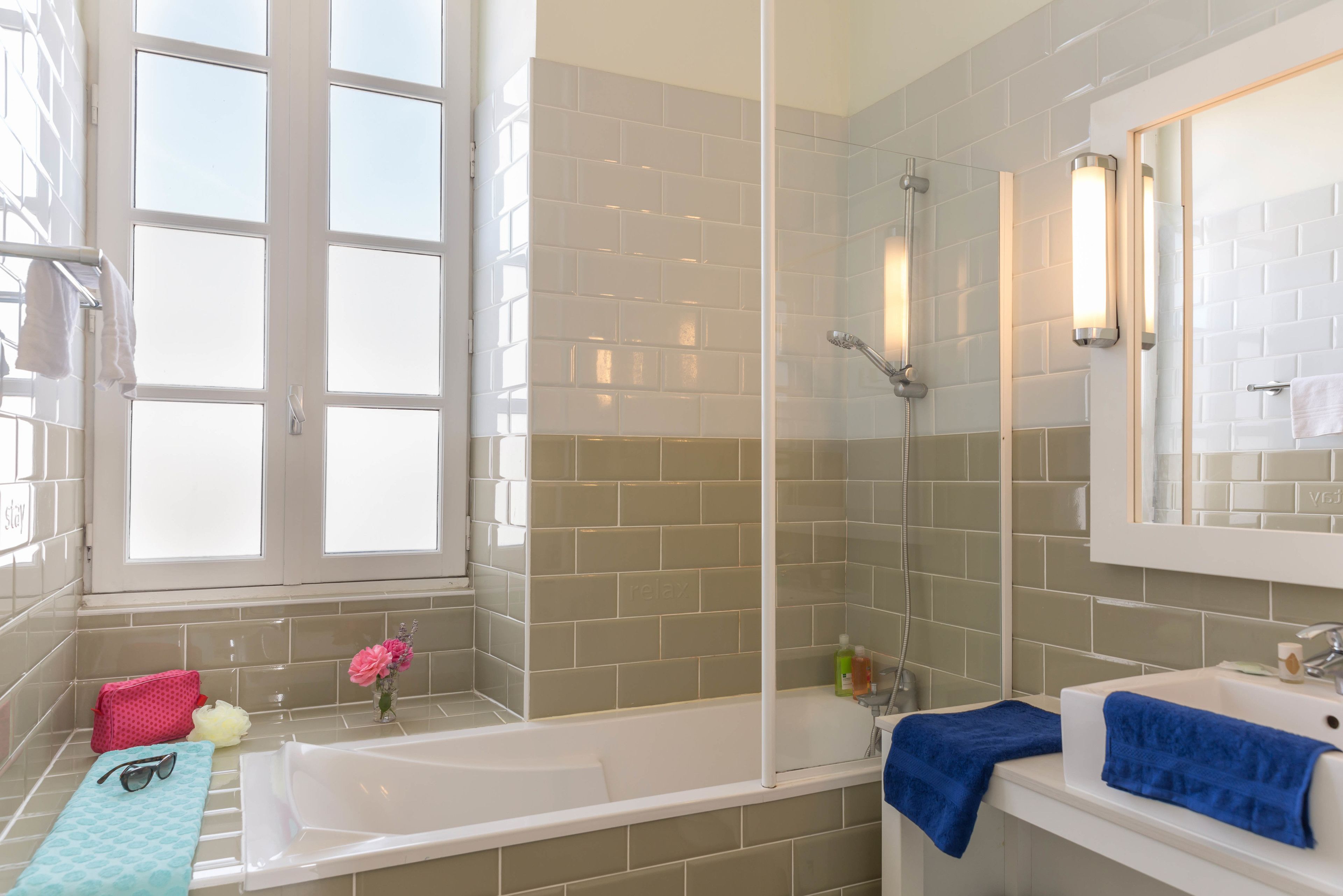 A bathroom with a bathtub, a sink, and a shower. There is a window with a view of the outside, and a towel rack with towels.